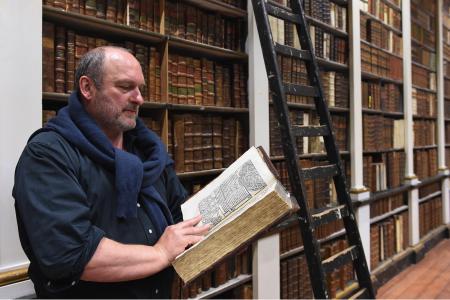 Yves Charlier, directeur de la Bibliothèque du séminaire de Liège, parcourt un livre ancien dans un rayonnage de la bibliothèque.